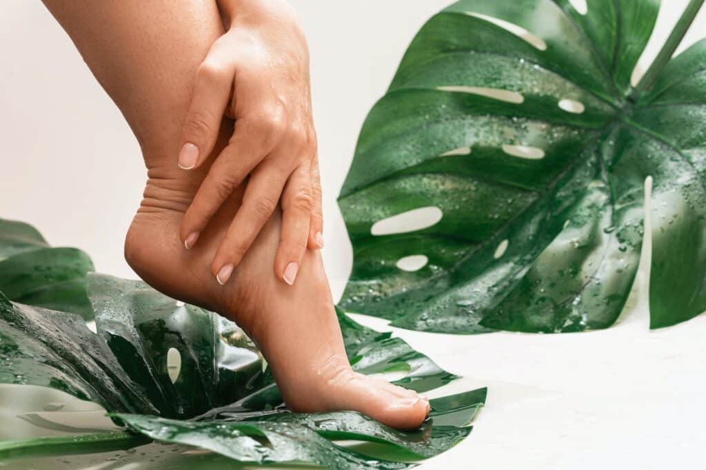 Wet female feet with smooth skin and Monstera deliciosa tropical leaf